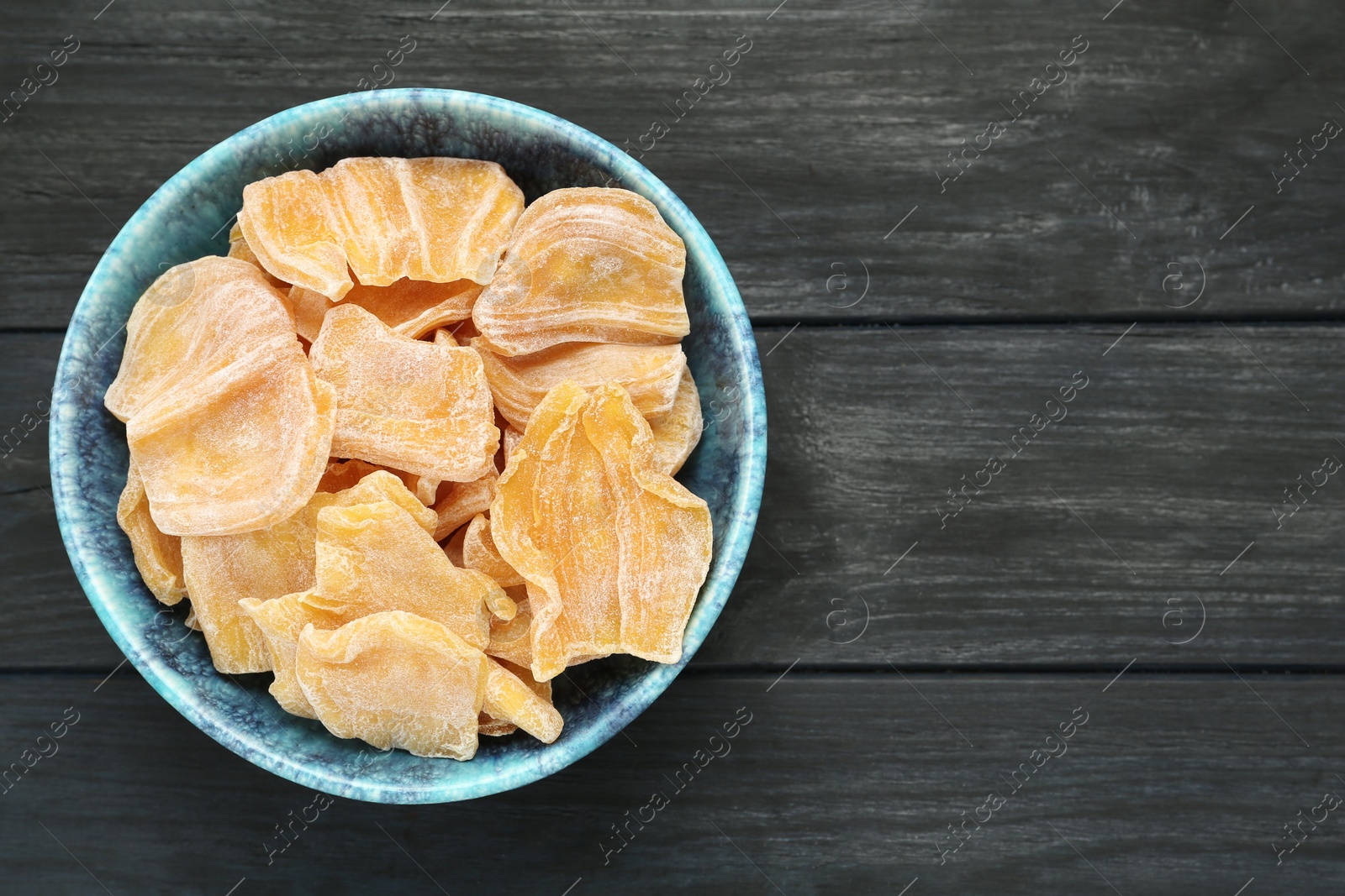 Photo of Delicious dried jackfruit slices in bowl on black wooden table, top view. Space for text