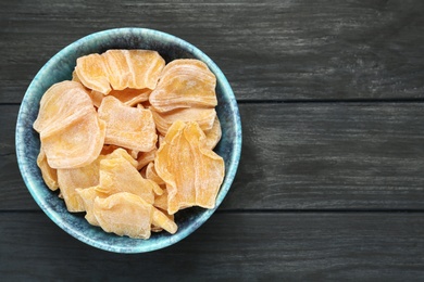 Photo of Delicious dried jackfruit slices in bowl on black wooden table, top view. Space for text