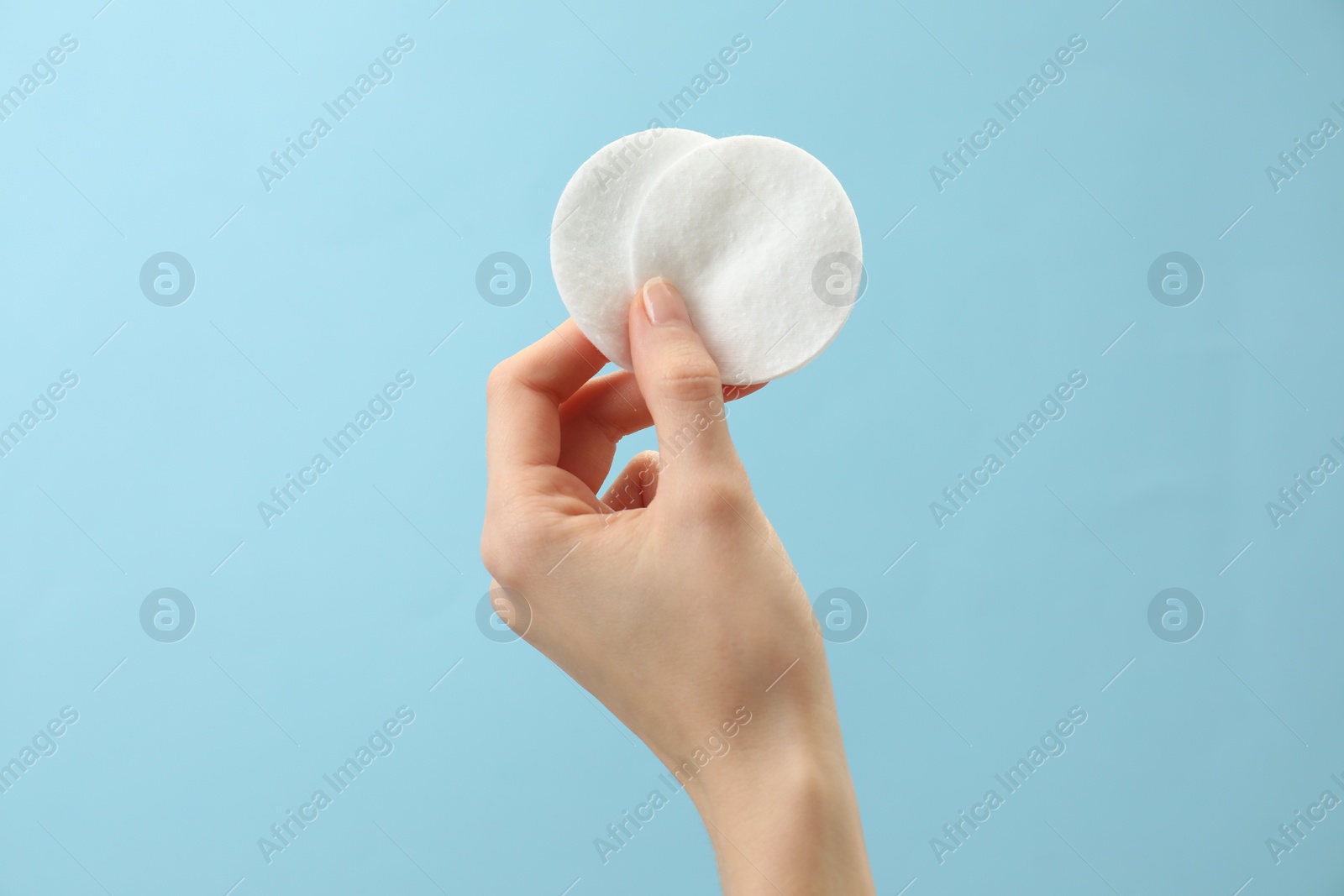 Photo of Woman holding cotton pads on light blue background, closeup