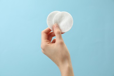 Woman holding cotton pads on light blue background, closeup