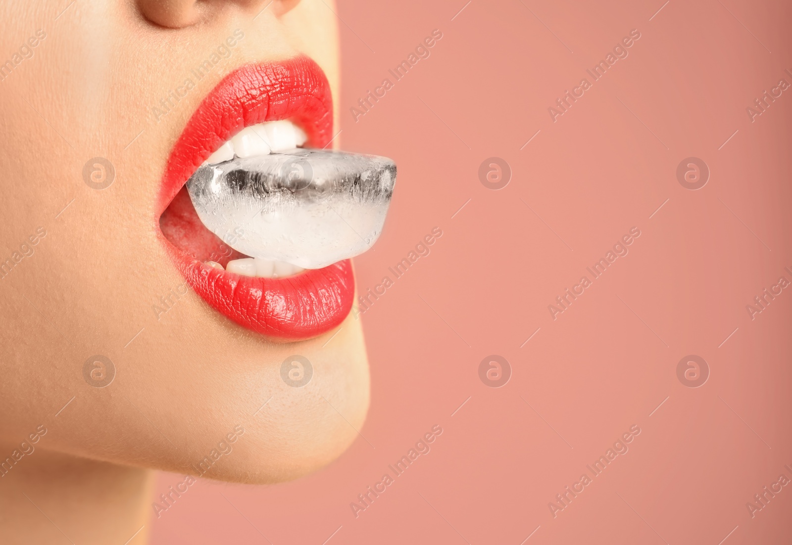 Photo of Young woman holding ice cube in mouth on color background, closeup. Space for text