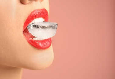 Young woman holding ice cube in mouth on color background, closeup. Space for text