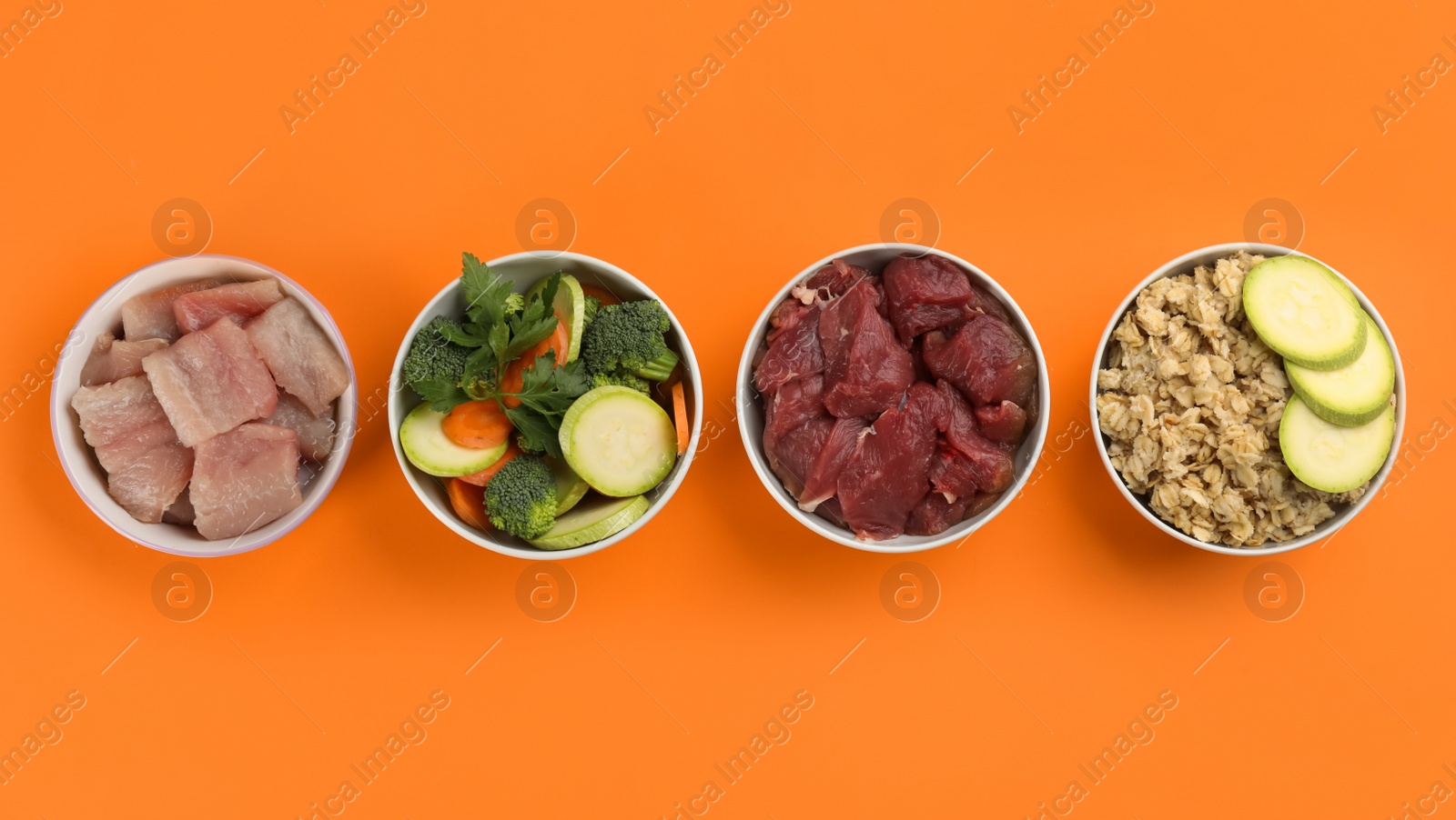 Photo of Feeding bowls with natural pet food on orange background, flat lay