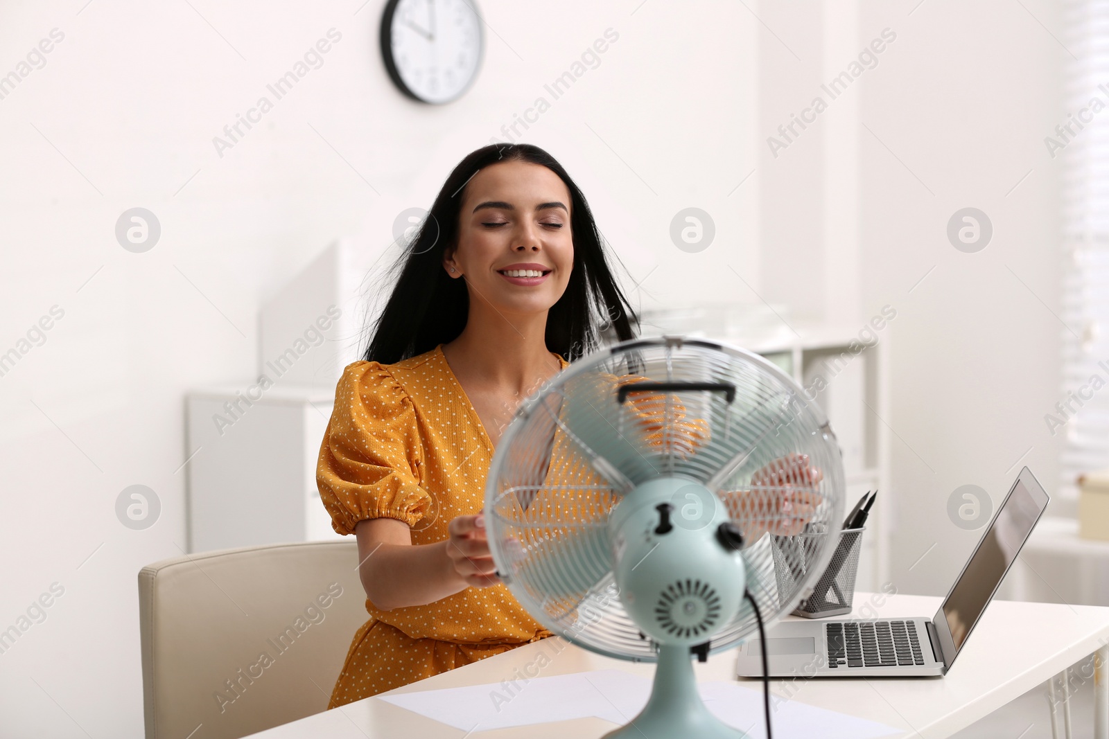 Photo of Young woman enjoying air flow from fan at workplace