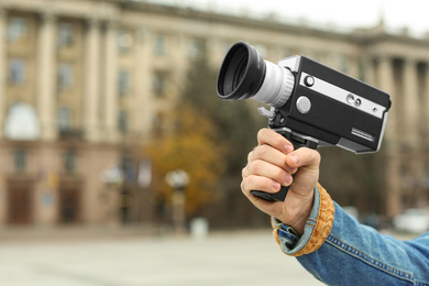 Photo of Young man with vintage video camera on city street, closeup of hand. Space for text