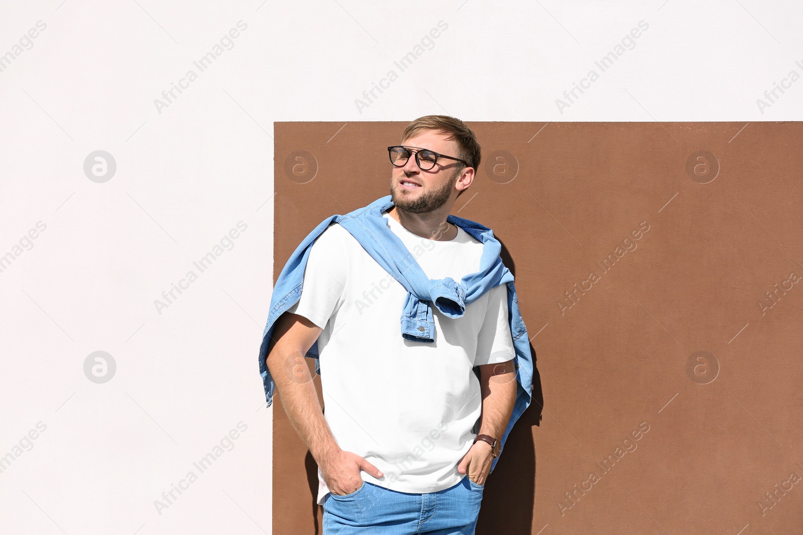 Photo of Young hipster man in stylish jeans posing near color wall