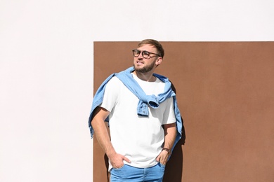 Young hipster man in stylish jeans posing near color wall