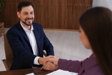 Photo of Office employees shaking hands over table with documents at workplace