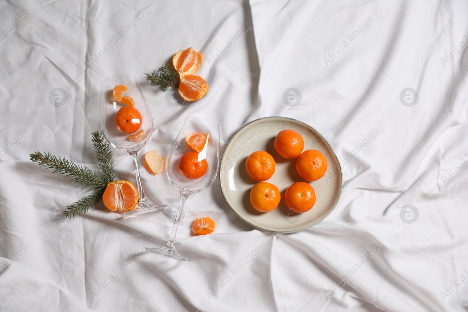 Photo of Delicious fresh ripe tangerines and glasses on white bedsheet, flat lay