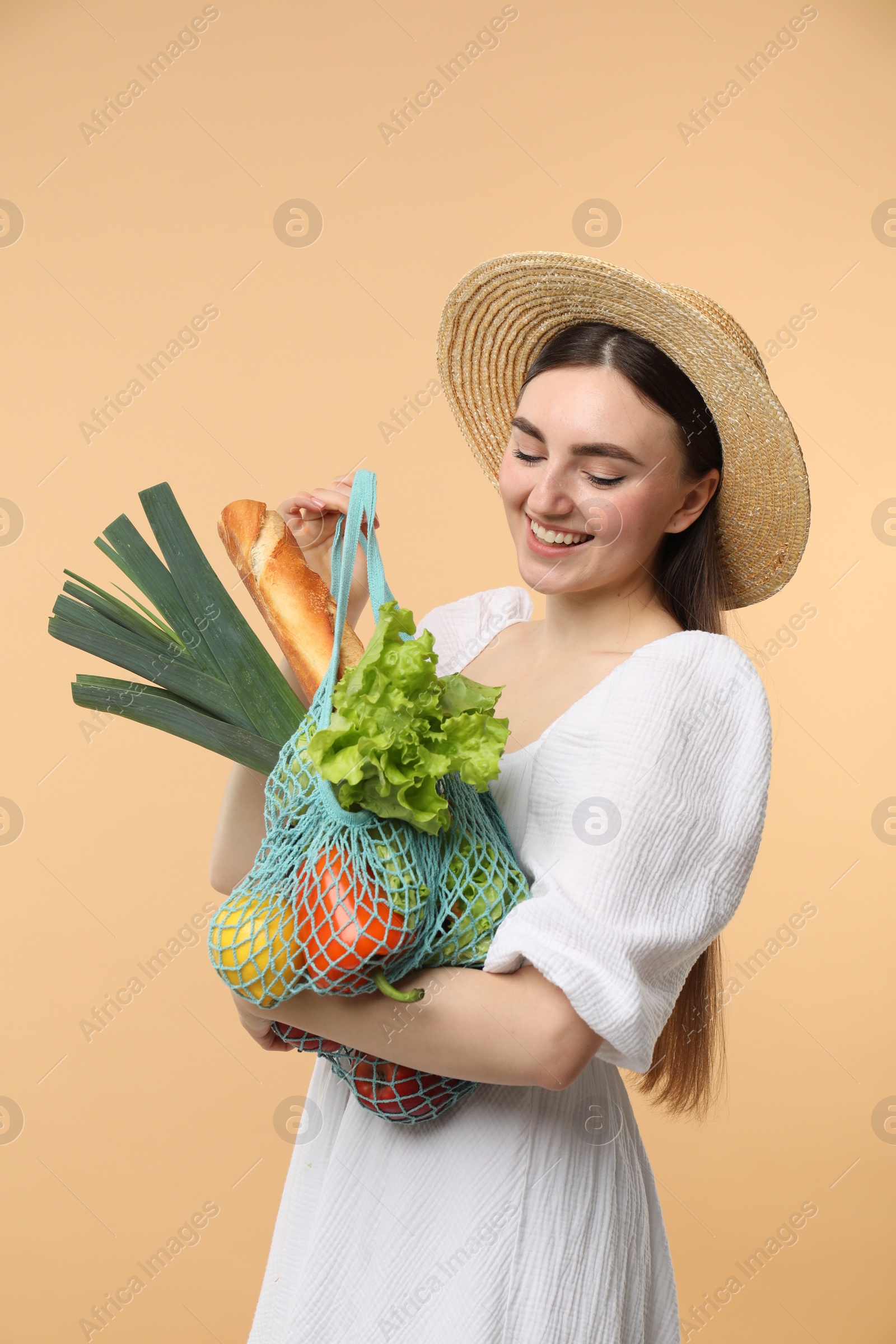 Photo of Woman with string bag of fresh vegetables and baguette on beige background