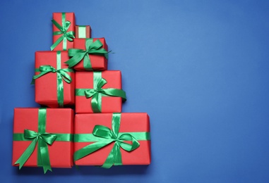 Photo of Christmas tree shape of gift boxes on blue background, flat lay. Space for text