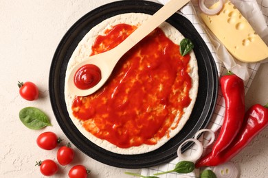 Pizza base smeared with tomato sauce and products on light textured table, flat lay