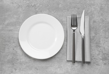 Photo of Clean plate and shiny silver cutlery on light grey table, flat lay