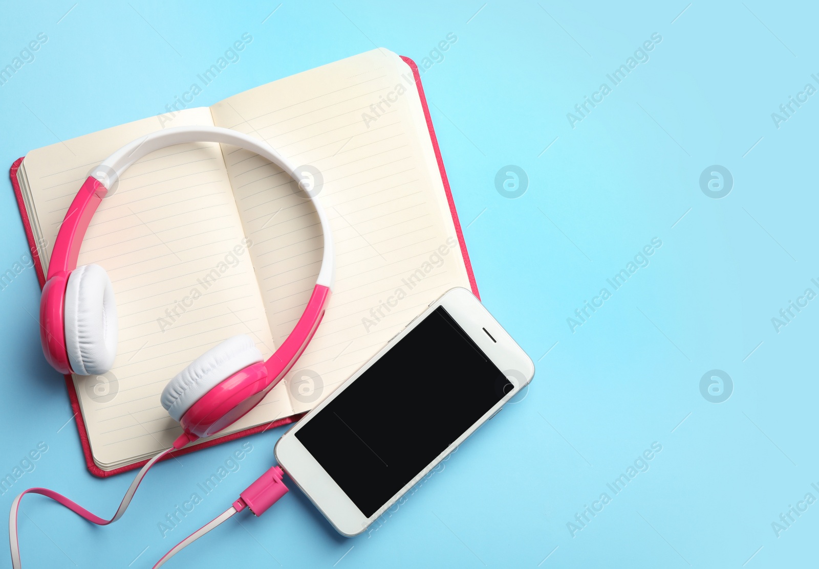 Photo of Modern headphones, phone and open notebook on color background, flat lay. Space for text