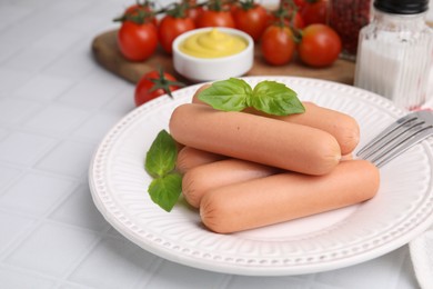 Photo of Delicious boiled sausages and basil served on white tiled table, closeup