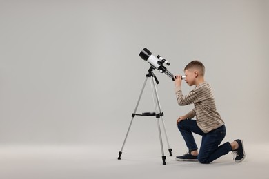 Photo of Little boy looking at stars through telescope on light grey background, space for text