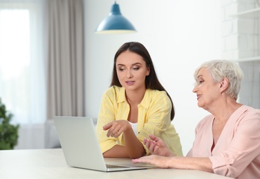 Photo of Young woman helping her mother to use laptop at home