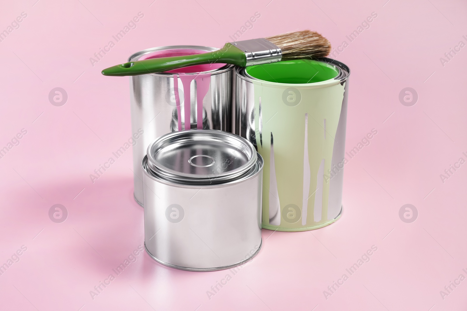 Photo of Cans of paints and brush on pink background