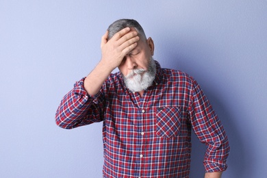 Mature man suffering from headache on color background