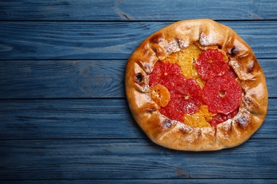 Photo of Delicious galette with citrus fruits on blue wooden table, top view. Space for text