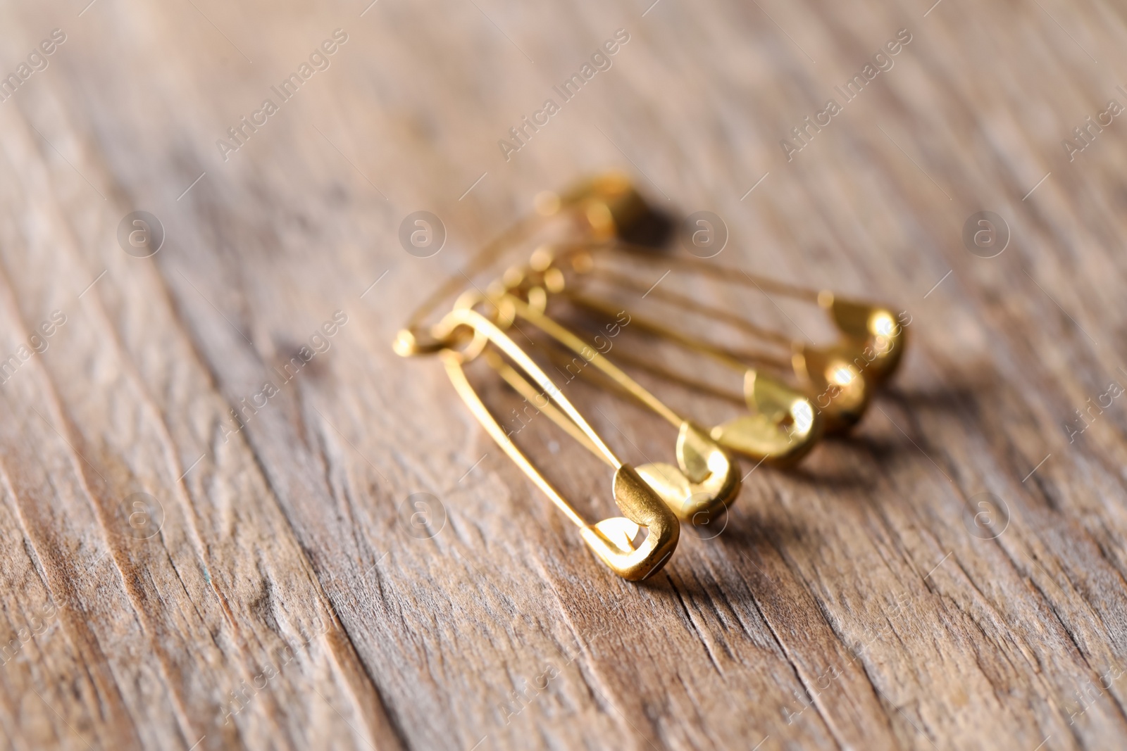 Photo of Golden safety pins on wooden table, closeup. Space for text