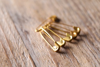 Golden safety pins on wooden table, closeup. Space for text