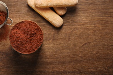 Photo of Delicious tiramisu in glass, biscuits and cocoa powder on wooden table, flat lay. Space for text