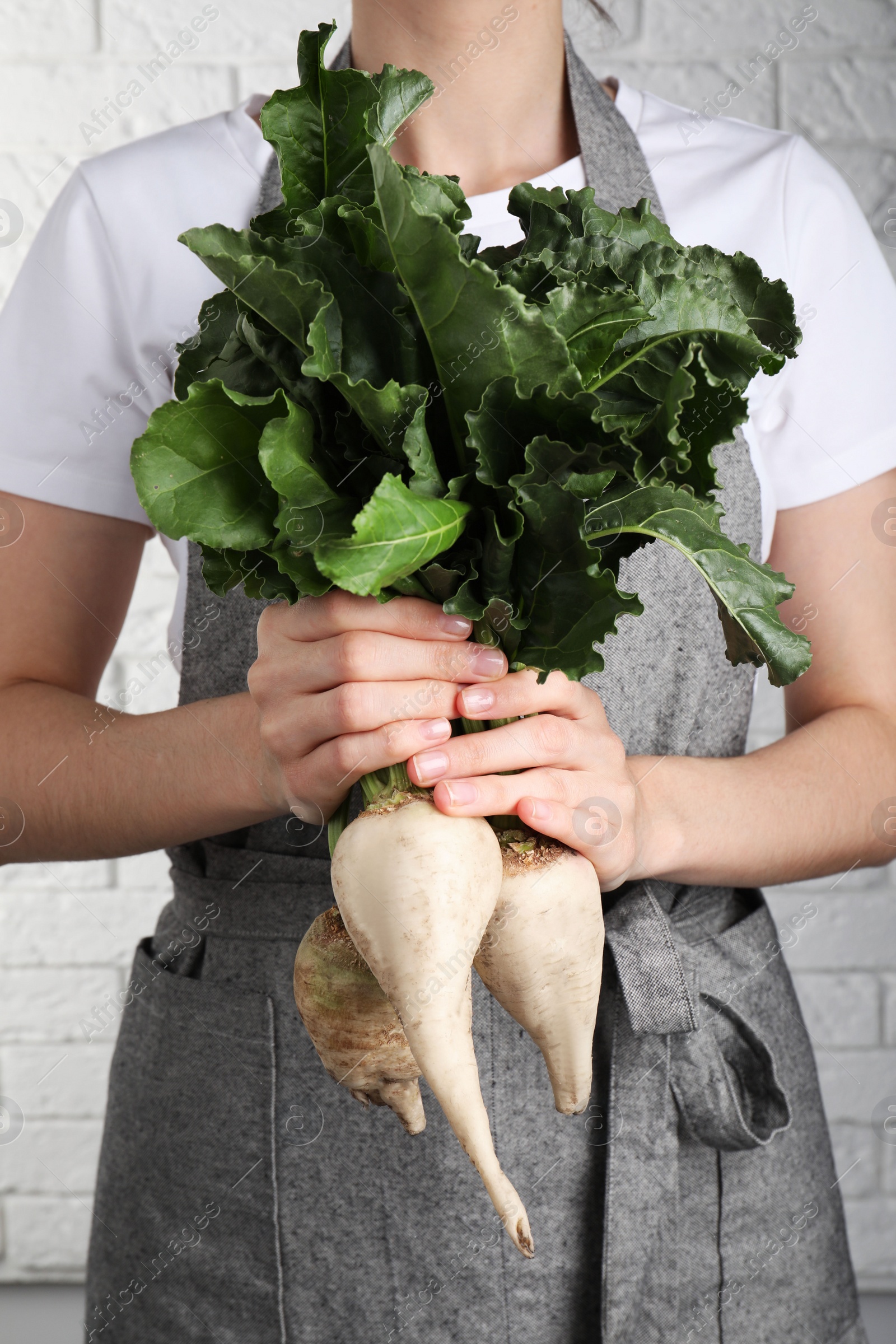 Photo of Woman holding sugar beets against white brick wall, closeup