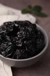Photo of Sweet dried prunes in bowl on brown table, closeup