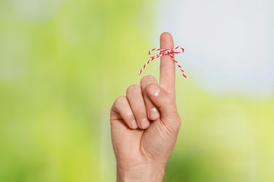 Photo of Man showing index finger with tied bow as reminder on green blurred background, closeup
