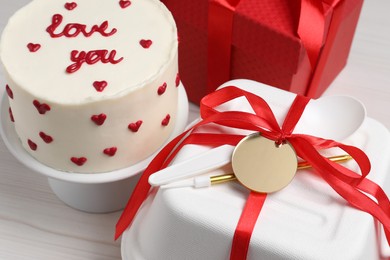 Photo of Bento cake with text Love You, gift box and takeaway packaging on white wooden table. St. Valentine's day surprise