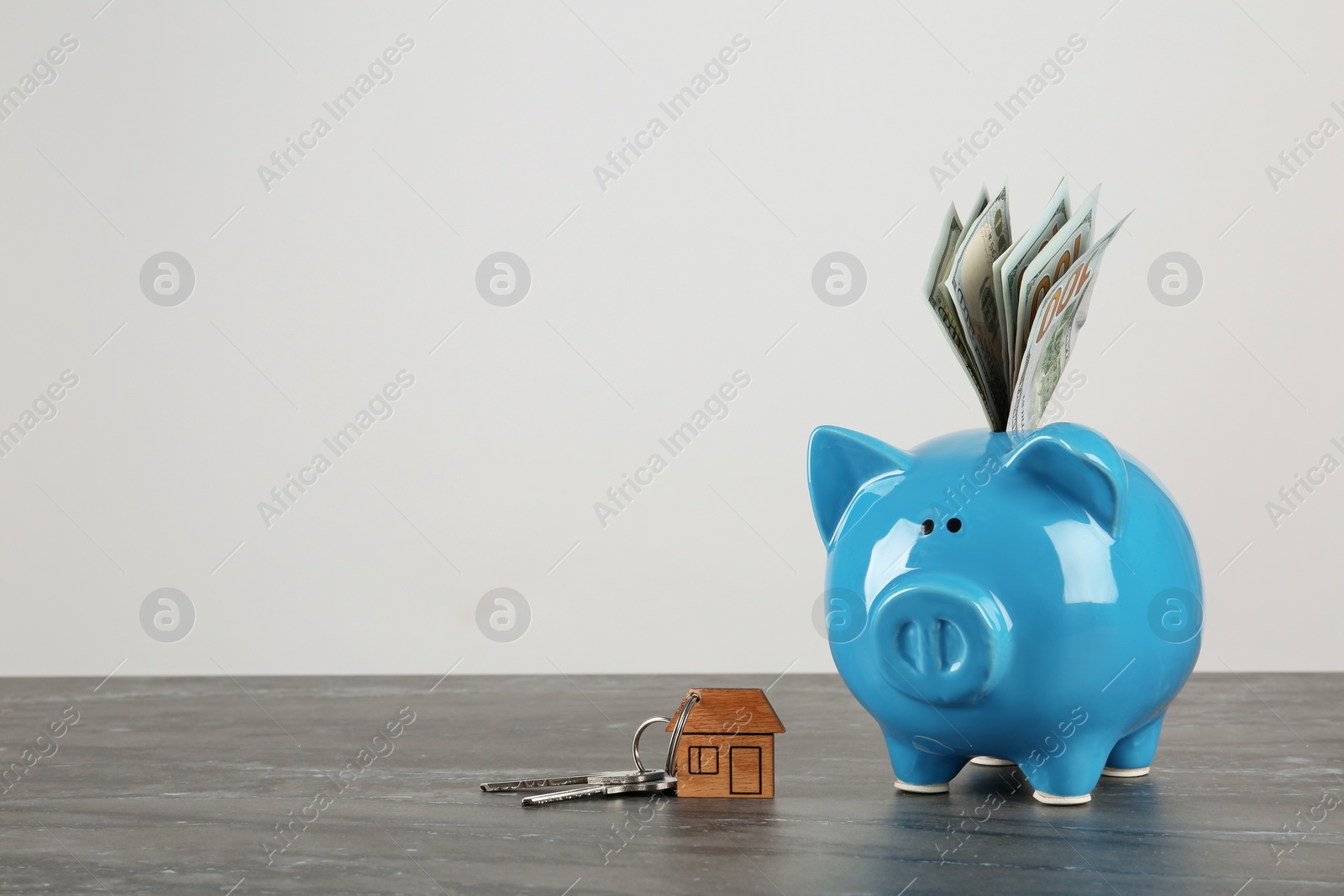 Photo of Piggy bank with dollar banknotes and house keys on table against white background. Space for text