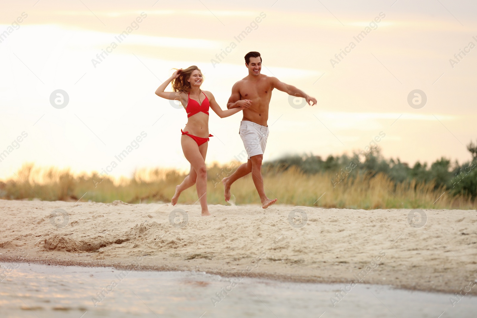 Photo of Happy young couple running together on sea beach at sunset