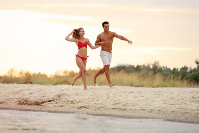 Happy young couple running together on sea beach at sunset