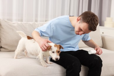 Photo of Pet shedding. Man with lint roller removing dog's hair from pants on sofa at home