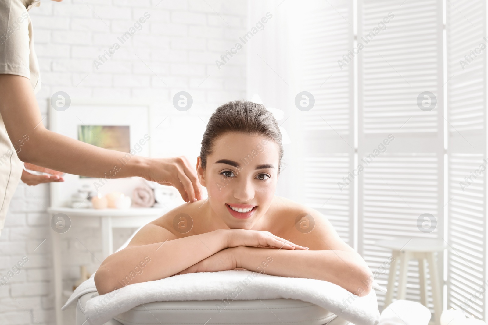 Photo of Young woman having body scrubbing procedure with sea salt in spa salon