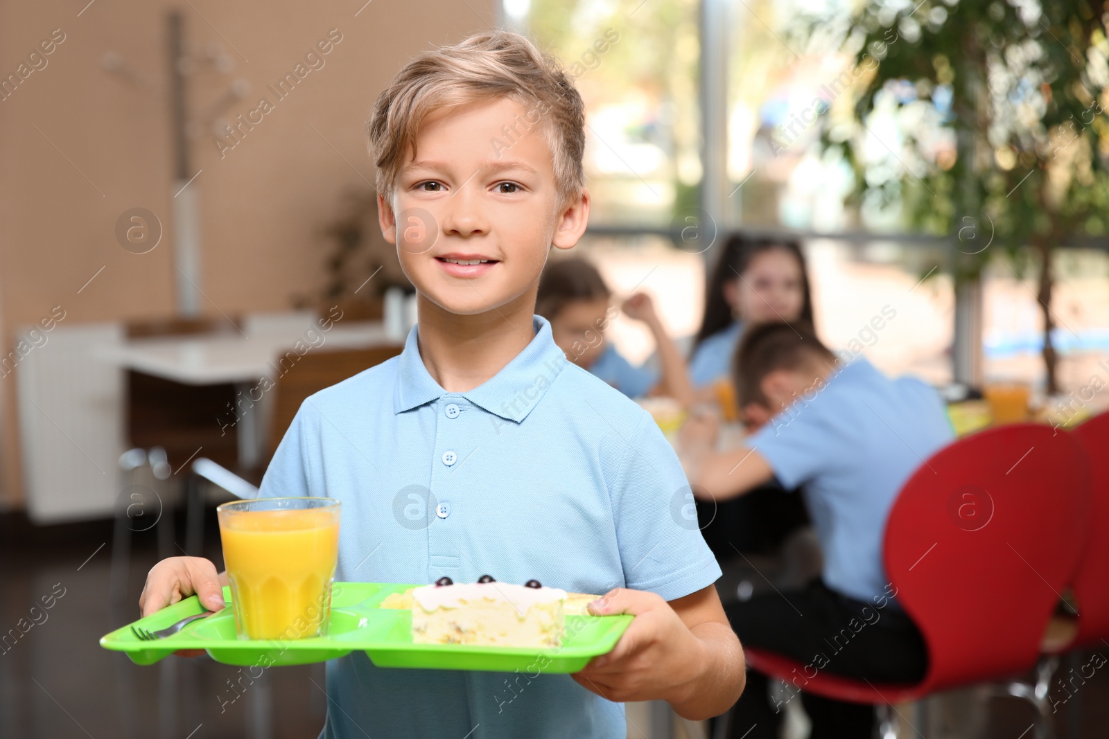 Photo of Cute boy holding tray with healthy food in school canteen