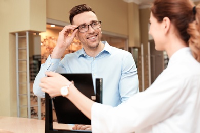 Female ophthalmologist helping man to choose glasses in optical store