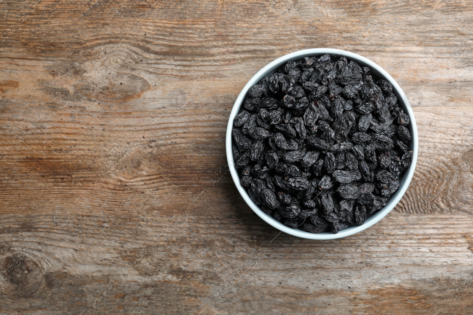 Photo of Bowl with raisins and space for text on wooden background, top view. Dried fruit as healthy snack