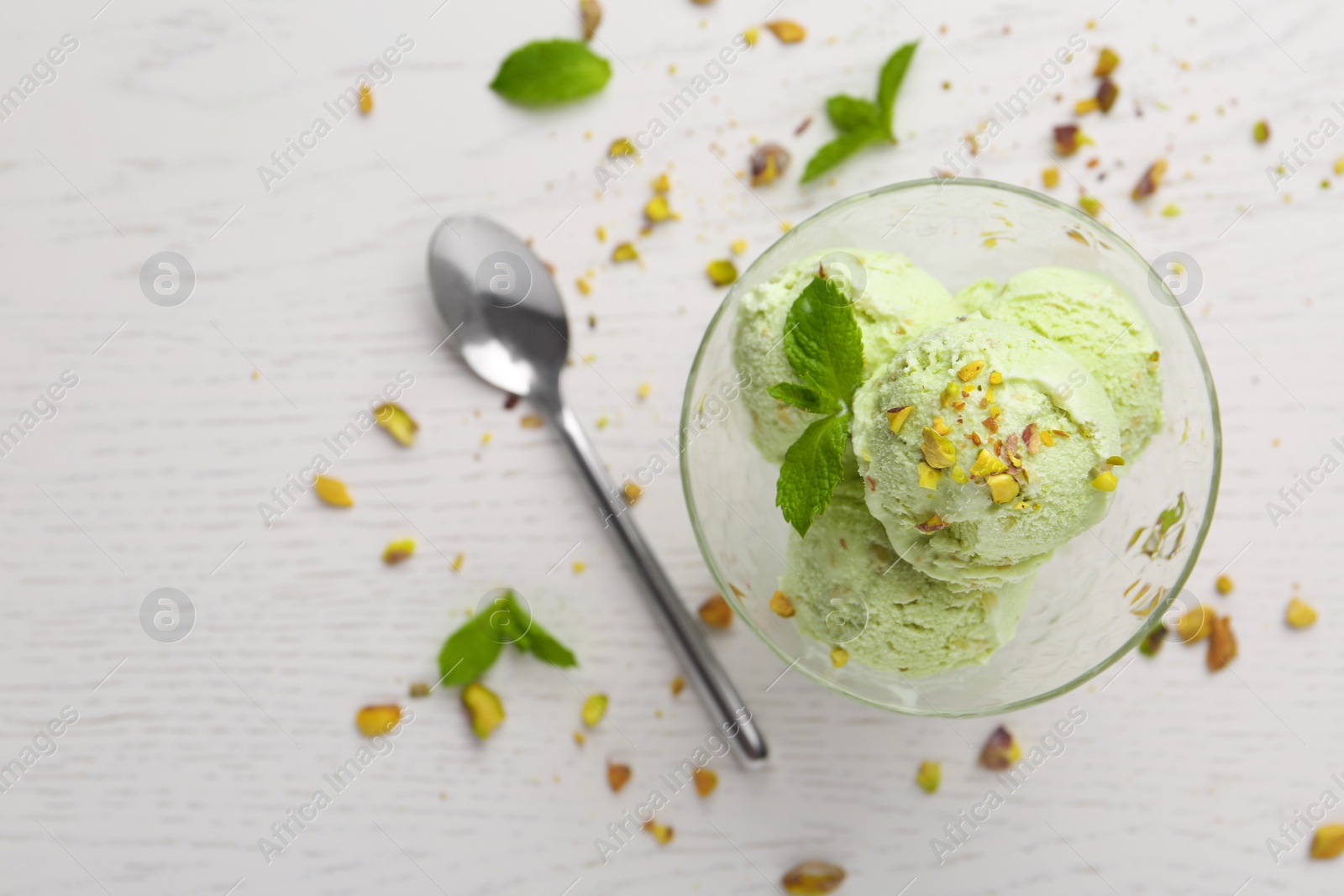 Photo of Delicious green ice cream served in dessert bowl on white wooden table, top view. Space for text