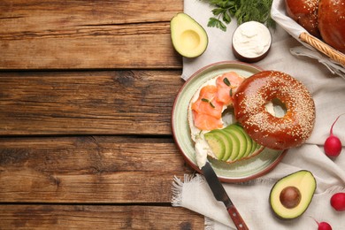 Delicious bagel with cream cheese, salmon and avocado on wooden table, flat lay. Space for text