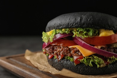 Photo of Board with black burger on dark background, closeup. Space for text