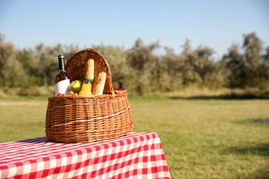 Wicker picnic basket with wine and snacks on table in park. Space for text