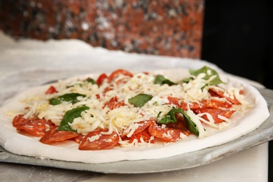 Peel with raw traditional Italian pizza on table in restaurant kitchen, closeup