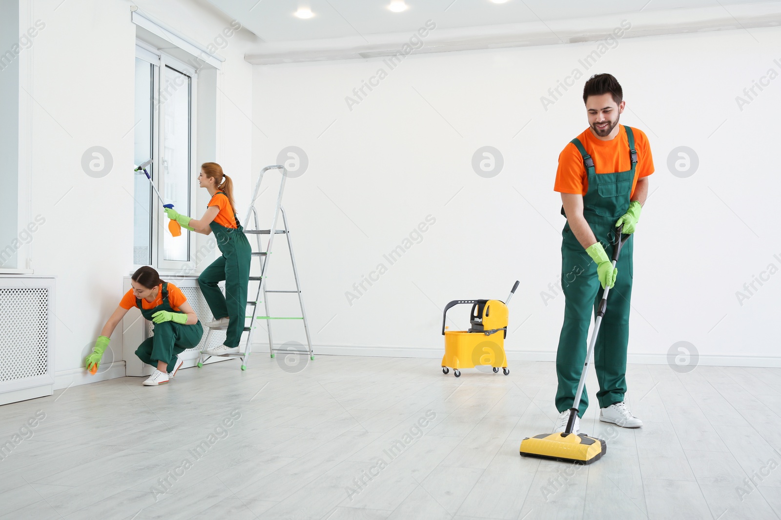 Photo of Team of professional janitors in uniforms cleaning room