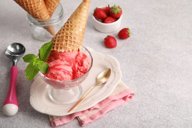 Photo of Delicious scoops of strawberry ice cream with mint and wafer cone in glass dessert bowl served on grey table. Space for text