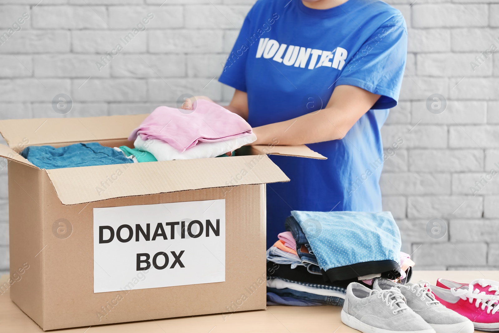 Photo of Female volunteer collecting clothes and shoes into donation box indoors