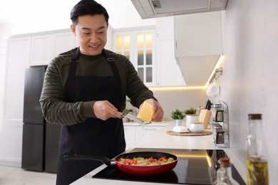 Photo of Cooking process. Man grating cheese into frying pan in kitchen