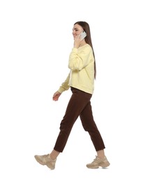 Young woman in casual outfit talking on smartphone while walking against white background