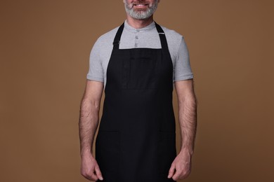 Man wearing kitchen apron on brown background, closeup. Mockup for design